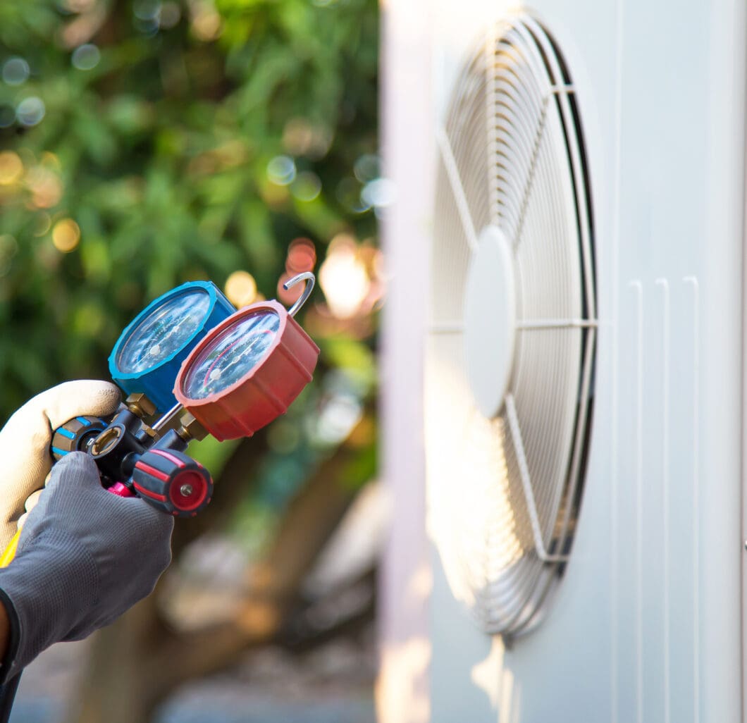 HVAC technician holding pressure gauges in front of an air conditioning unit, illustrating professional service for heating and cooling solutions in Tempe, AZ.