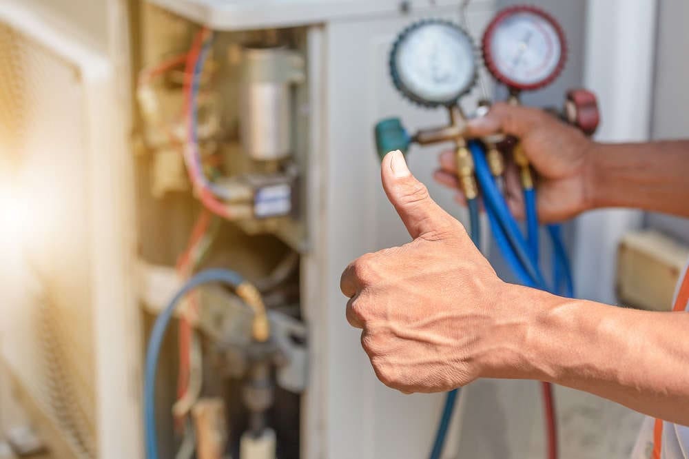Technician performing maintenance on an air conditioning unit, showing a thumbs up, symbolizing successful service and readiness for A2L refrigerant transition.